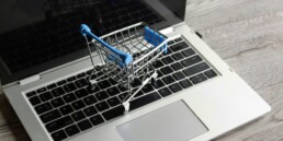Laptop and mini shopping trolley on wooden table. Online shopping concept
