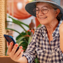 Happy senior woman with hat and eyeglasses holding smartphone