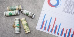 A flat lay of rolled dollar bills and a paper with charts - finances